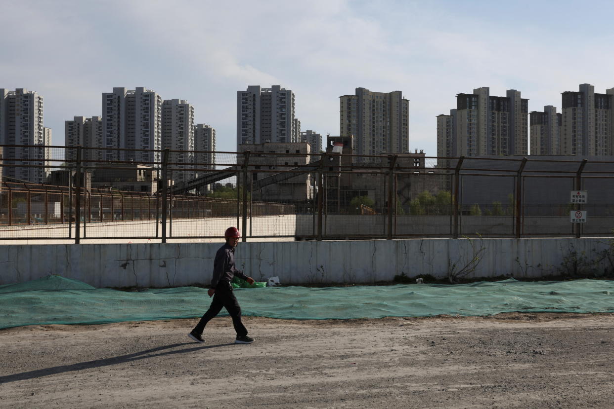  A worker walks past a construction site near a skyline of tall residential buildings.