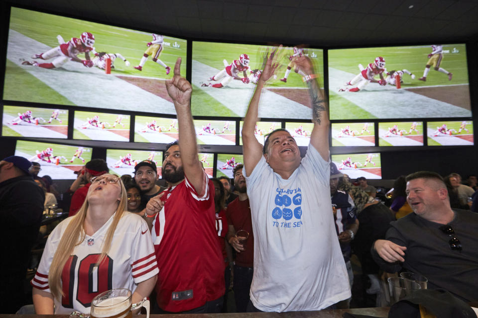 FILE - In this Feb. 2, 2020, file photo, Lazaro Real Cruz, center right, reacts as Kansas City Chiefs' Damien Williams scores a touchdown against the San Francisco 49ers during the second half of the NFL Super Bowl 54 football game while watching TV at Tom's Watch Bar LA Live in Los Angeles. Let's get this straight from the outset: If the NFL has no fans at any games this season _ or doesn't have much of a season at all _ it will not go out of business. Sure, the 32 teams and the league itself will lose millions, very possibly billions of dollars. Its broadcast partners will take a hit harder than any that Von Miller has delivered on the field. Same for sponsors and advertisers who pinpoint pro football as the best way to reach fans (read: consumers). (AP Photo/Damian Dovarganes, File)