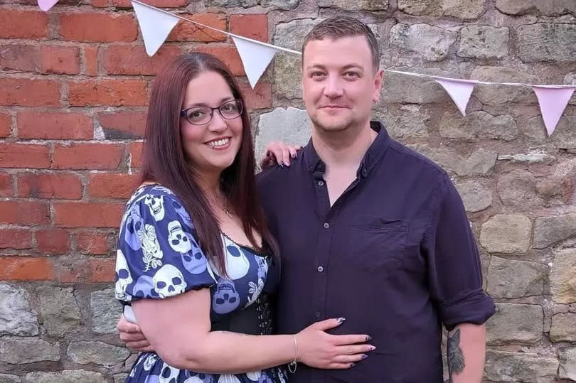 Woman and man stand closely in front of a wall