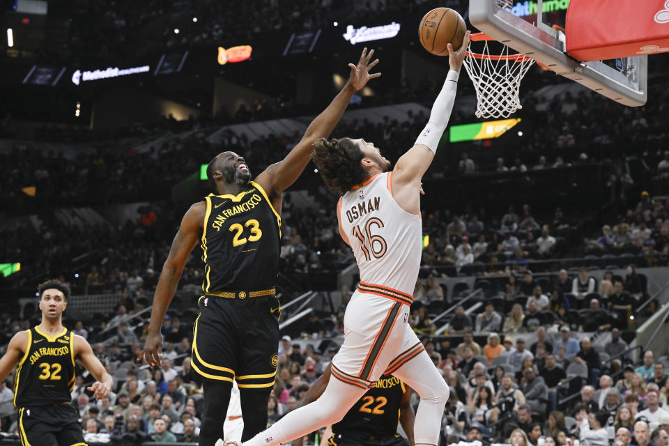 San Antonio Spurs' Cedi Osman (16) goes to the basket against Golden State Warriors' Draymond Green during the first half of an NBA basketball game, Sunday, March 31, 2024, in San Antonio. (AP Photo/Darren Abate)
