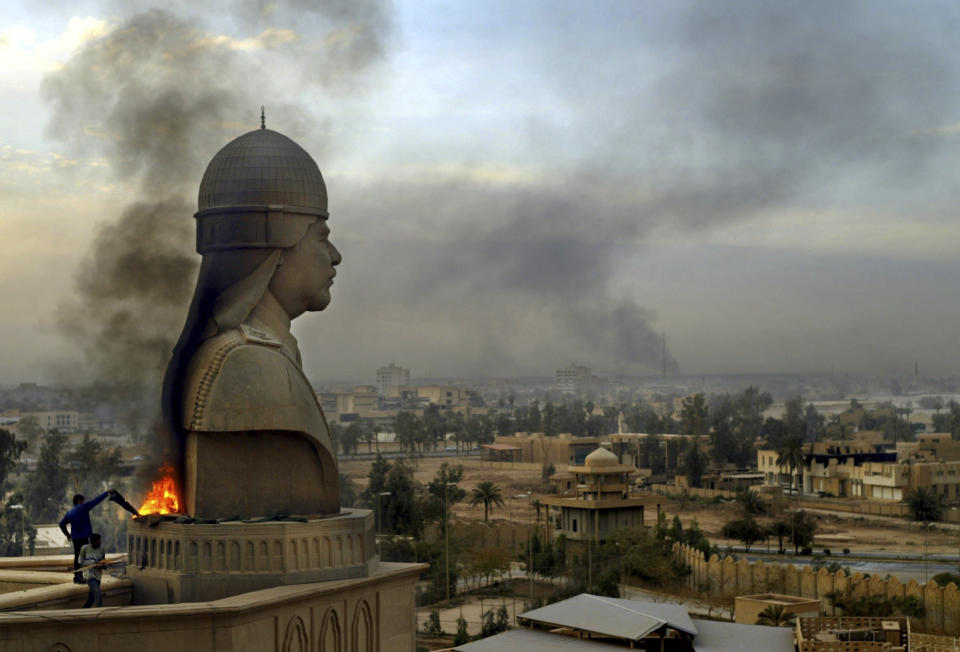 File - Smoke billows from the base of a sculpture depicting Iraqi President Saddam Hussein after looters set it on fire atop the roof of his Al-Salam Presidential Palace in Baghdad, Sunday, April 13, 2003. (AP Photo/Lefteris Pitarakis, File)