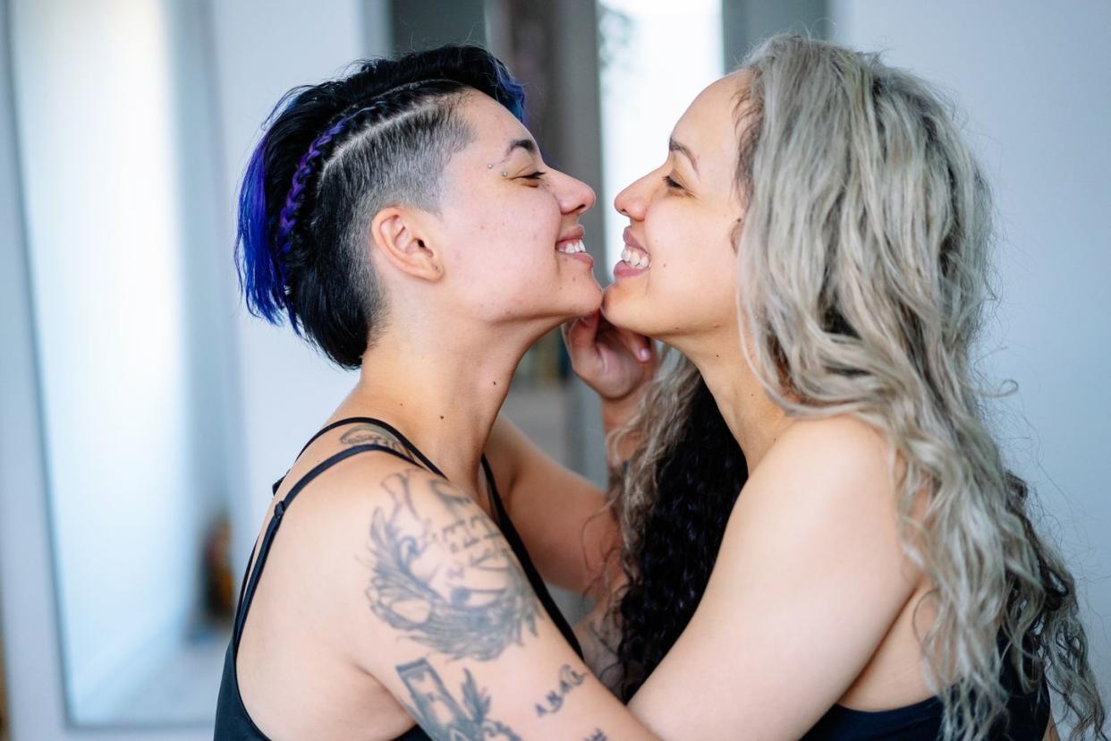 portrait of hispanic lesbian women kissing with tenderness in bedroom with tattoo
