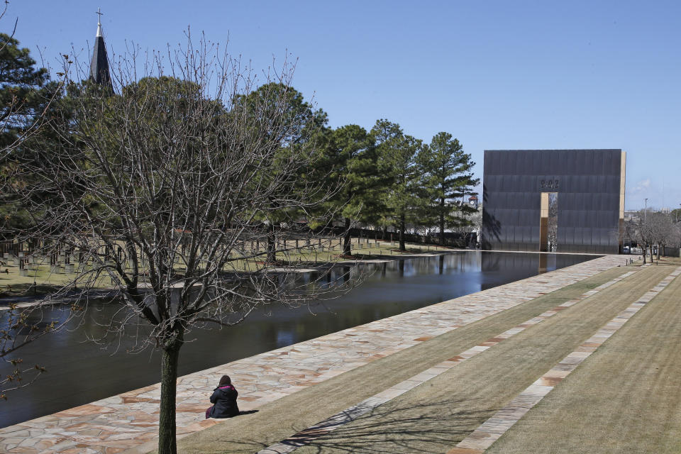 FILE - In this March 18, 2020 file photo, a visitor sits next to the reflecting pool at the Oklahoma City National Memorial and Museum in Oklahoma City. The Oklahoma City National Memorial and Museum has announced that it will offer a recorded, one-hour television program in place of a live ceremony to mark the 25th anniversary of the Oklahoma City bombing due to concerns about the spread of the coronavirus. (AP Photo/Sue Ogrocki, File)