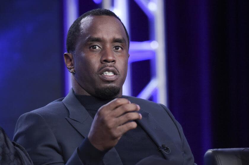 Sean 'Diddy' Combs is seated in a suit and motions with his right hand