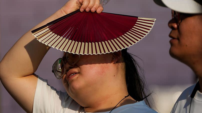 A woman uses a fan as she walks with her companion on a hot day in Beijing, 16 June 2024. June 2024 was the hottest June on record, according to Copernicus.