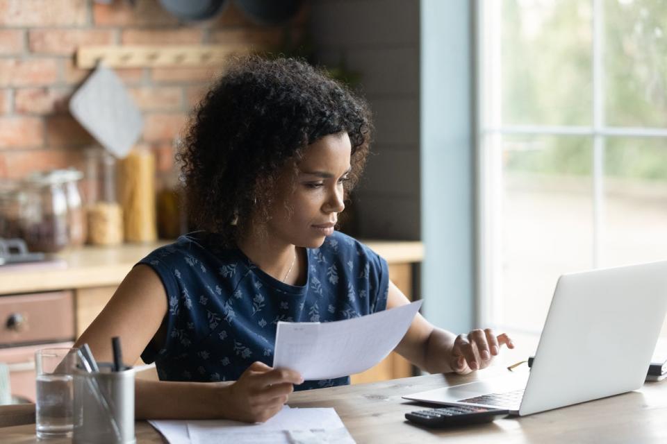 A woman looks at a document while scrolling a computer. 