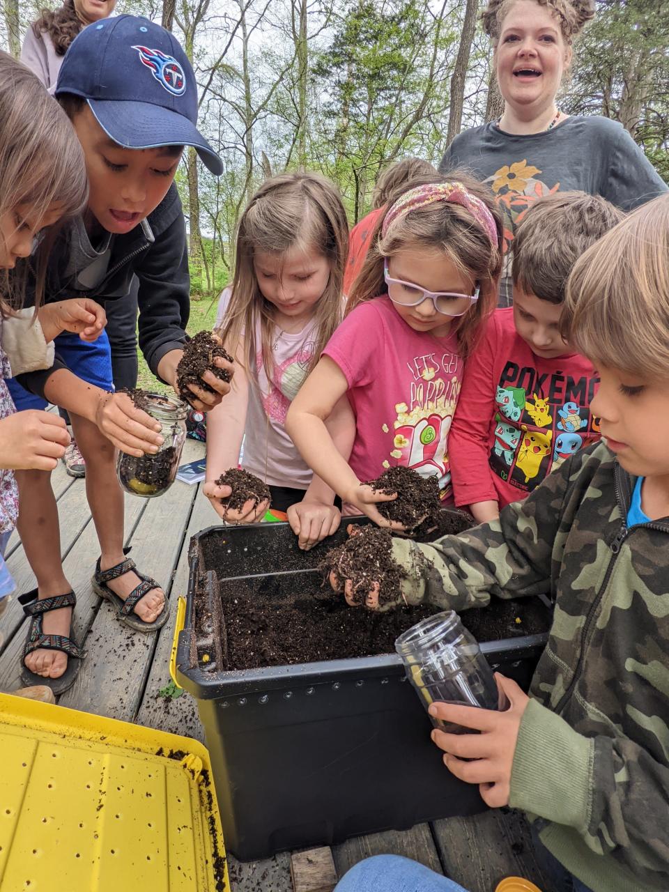 Forest School participants (from left) Gabriella Soreano, Asher Soreano, Maddie Singleton, Freya Therrien, Aiden Therrien and Tyberius Julian, along with Lauren King (back), gather red wiggler worms for their compost worm jars.