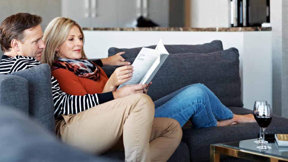 Shot of a mature couple reading a book together on their living room sofa.