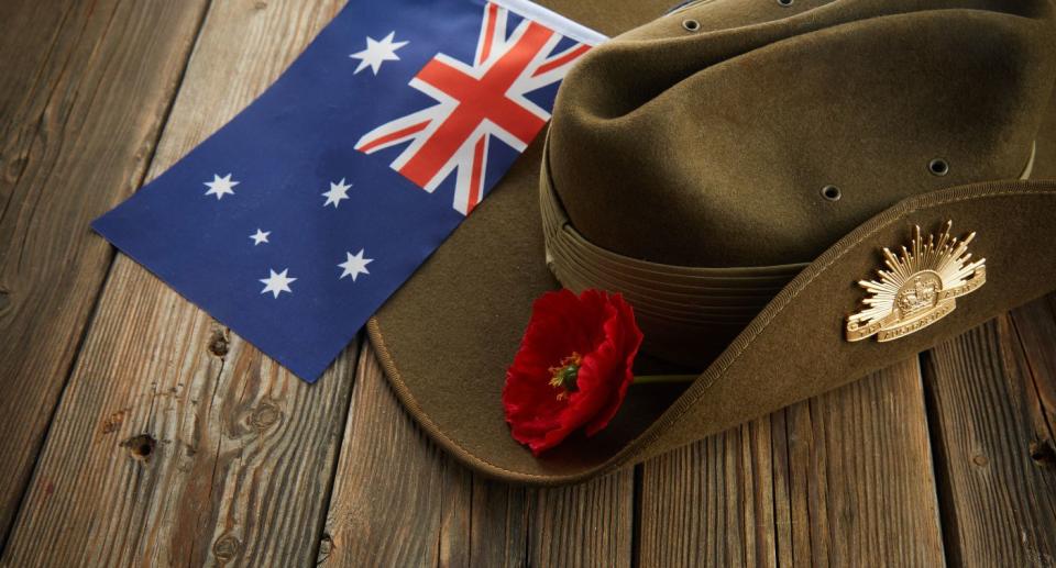 Australian flag, digger's hat and poppy lying on a wooden table.