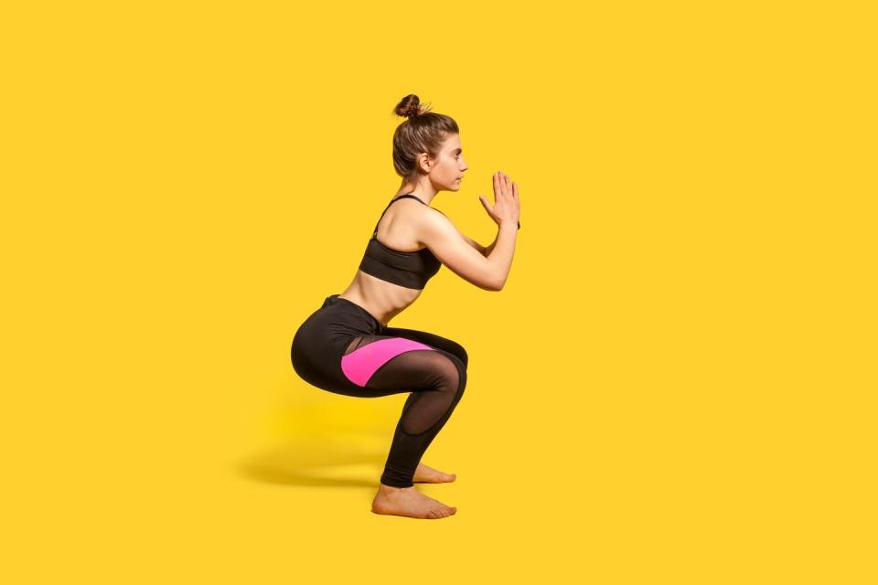 athletic woman with hair bun in tight sportswear doing squat, lower body sport exercise, keeping balance