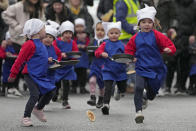 Schoolchildren from local schools take part in the children's races prior to the annual Pancake race in the town of Olney, in Buckinghamshire, England, Tuesday, Feb. 13, 2024. Every year women clad in aprons and head scarves from Olney and the city of Liberal, in Kansas, USA, run their respective legs of the race with pancakes in their pans. According to legend, the Olney race started in 1445 when a harried housewife arrived at church on Shrove Tuesday still clutching her frying pan with a pancake in it. (AP Photo/Kin Cheung)