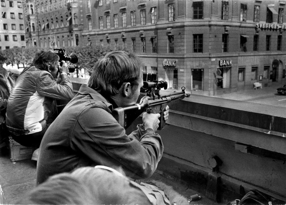 Press photographers and police snipers lie side-by-side on a roof opposite the Kreditbanken bank on Norrmalmstorg square in Stockholm on 24 August 1973. One of the hostages, Kristin Enmark, has said she feared being killed by police more than being harmed by the hostage-takers (AFP via Getty Images)