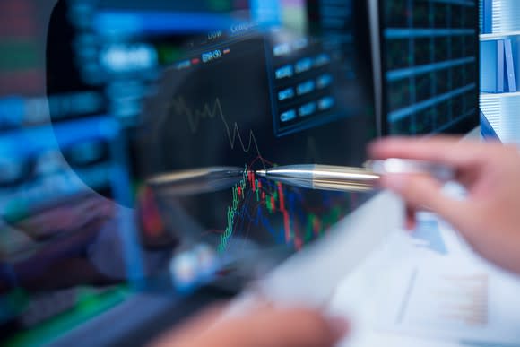 Person pointing to stock chart with a pen.