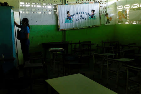 A teacher stands next to a billboard that reads "Welcome to classes" and empty desks in a classroom on the first day of school, in Caucagua, Venezuela September 17, 2018. REUTERS/Marco Bello
