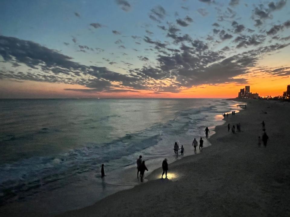 Beach goers stroll along the water's edge at dusk in Gulf Shores, Alabama on April 2, 2022.