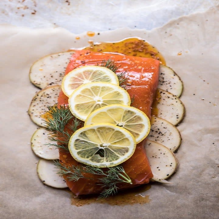 Salmon over a bed of potatoes on parchment paper.