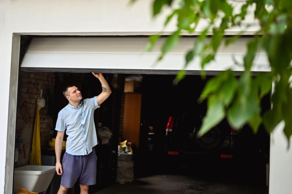 Young man with white shirt and blue shorts walks through attached car garage. 