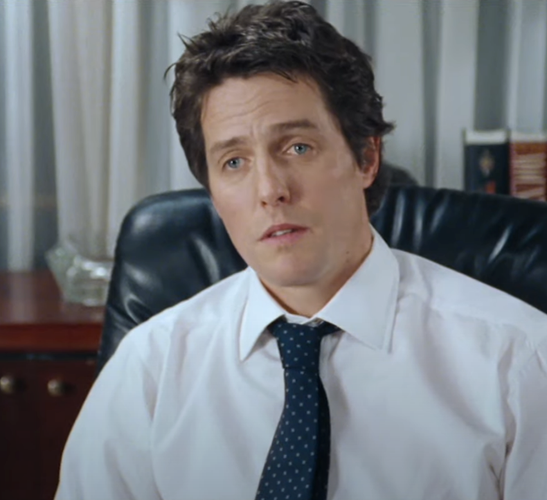 Hugh Grant sitting in an office chair