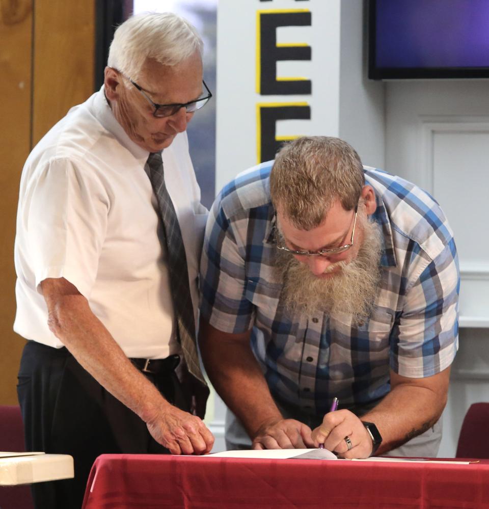 Attorney Kenneth Cardinal, left, looks on as Tim Nagy, right, trustee for Turning Point Baptist Church, signs papers during the Lexington Township Board of Trustees meeting Tuesday. After renting its building for 10 years, the church and the township finalized the purchase of the former Limaville Community Center.