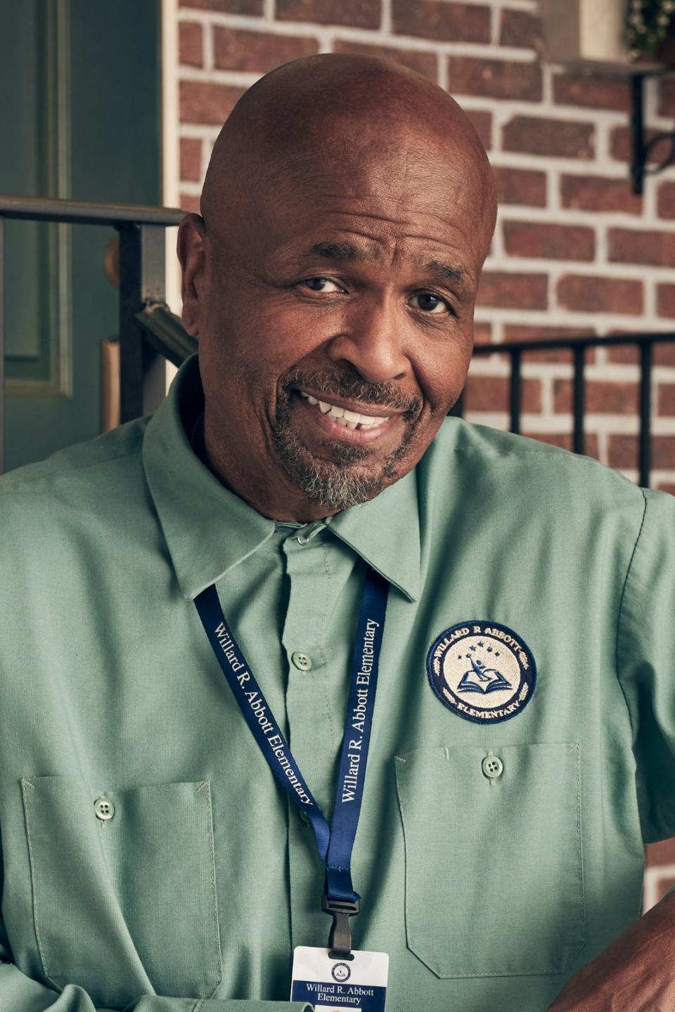 Smiling man in uniform with badge leaning on railing outside a building