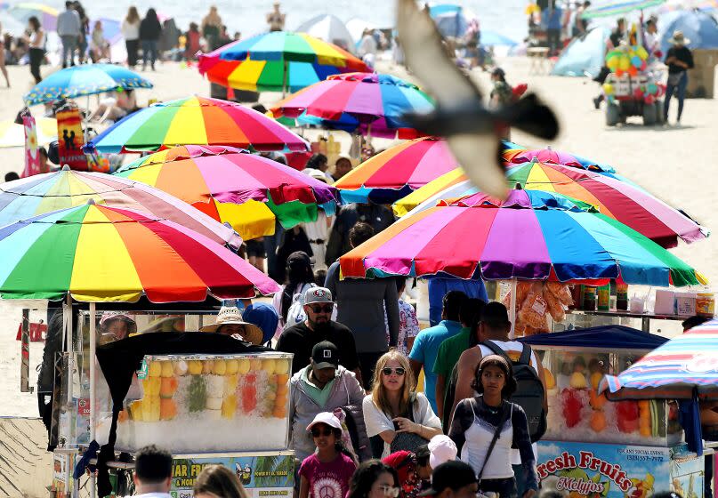 Santa Monica, CA - Beachghoers and snack vendors walk on Santa Monica Beach as the sun mometarily breaks through coastal clouds. A warming trend in Southern California is forecast to begin next week. (Luis Sinco / Los Angeles Times)