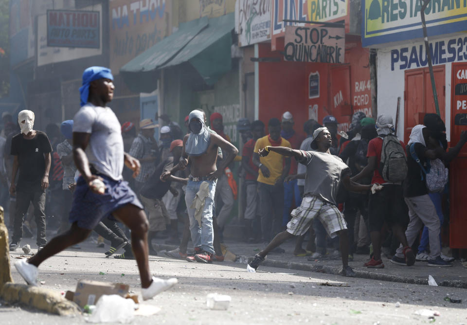 People throw rocks as others loot local businesses during anti-government protests in Port-au-Prince, Haiti, Friday, Oct. 11, 2019. Protesters burned tires and spilled oil on streets in parts of Haiti's capital as they renewed their call for the resignation of President Jovenel Moïse just hours after a journalist was shot to death. (AP Photo/Rebecca Blackwell)