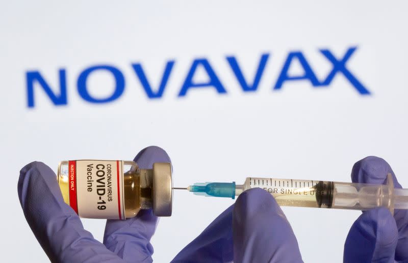 FILE PHOTO: A woman holds a small bottle labeled with a "Coronavirus COVID-19 Vaccine" sticker and a medical syringe in front of displayed Novavax logo in this illustration