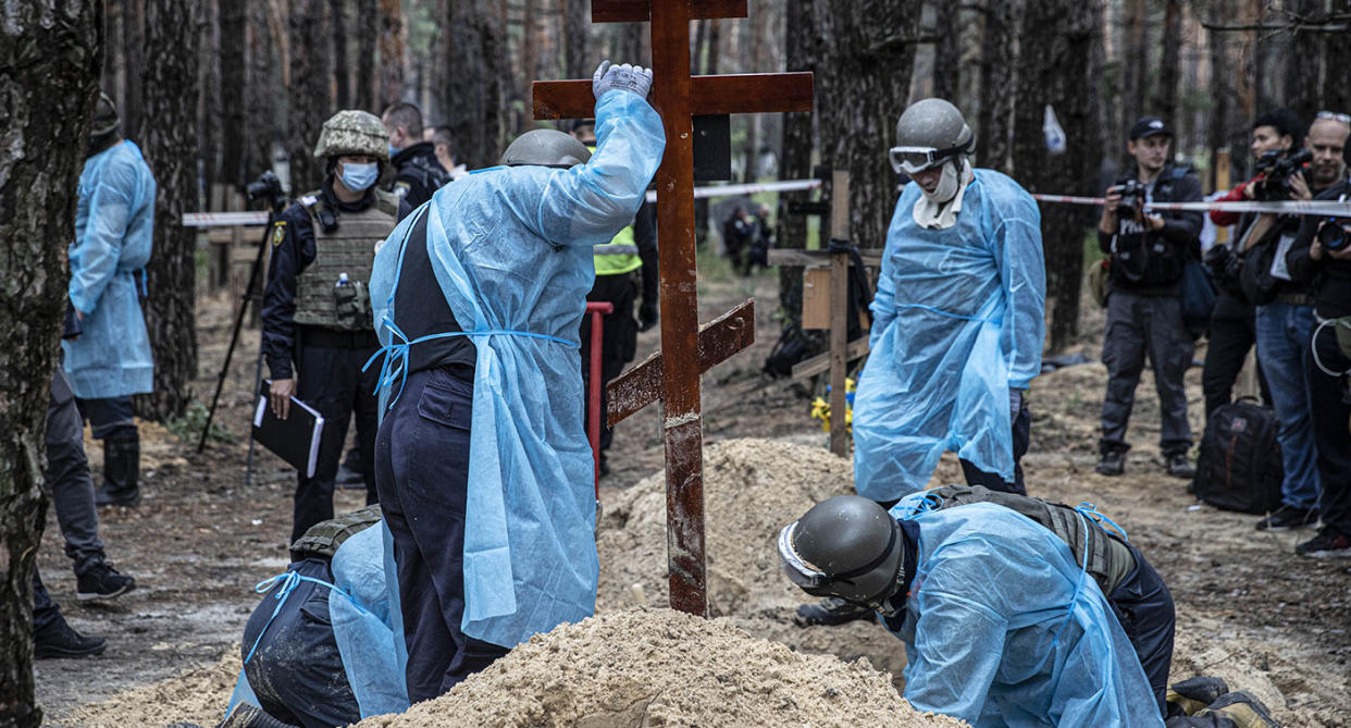 Ukrainian authorities in blue smocks work to exhume bodies buried in Izyum
