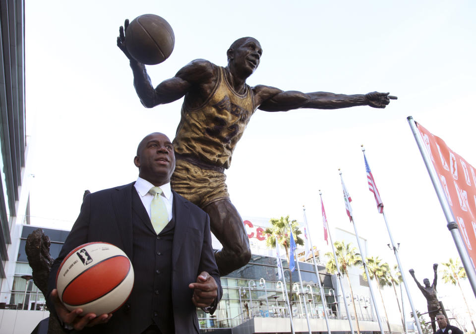 FILE - Former Los Angeles Lakers player Magic Johnson stands under a statue of himself after a news conference at the Staples Center in Los Angeles on Wednesday, Feb 5, 2014. The 19-foot, 4,000-pound statue of Kobe Bryant in downtown Los Angeles is just the latest example of a sports team honoring a player with this kind of larger-than-life presence.(AP Photo/Nick Ut, File)