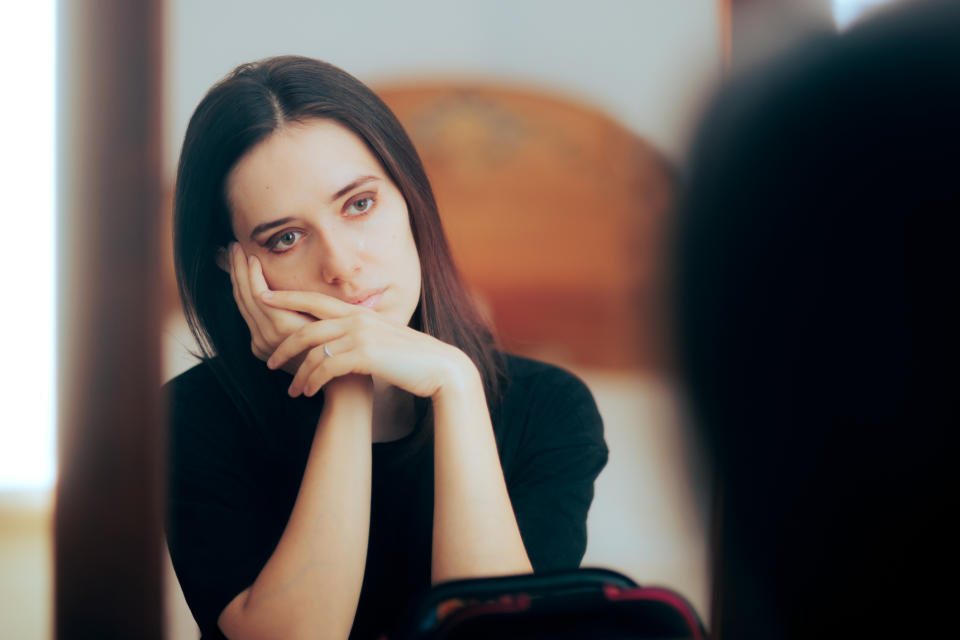 A woman cupping her cheek in front of her mirror