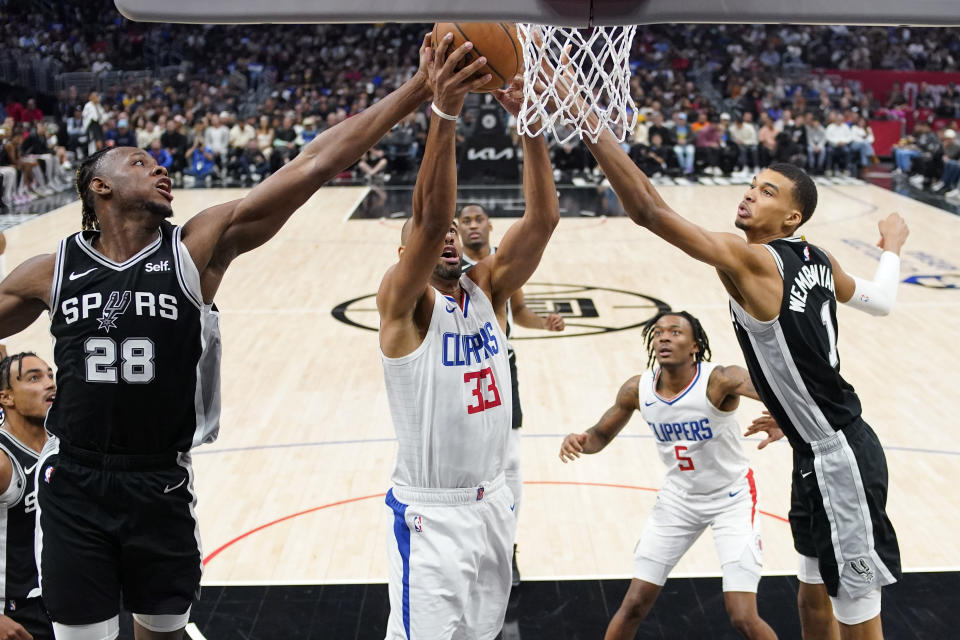 Los Angeles Clippers forward Nicolas Batum (33) grabs a rebound away from San Antonio Spurs center Charles Bassey (28) and center Victor Wembanyama (1) during the second half of an NBA basketball game Sunday, Oct. 29, 2023, in Los Angeles. (AP Photo/Mark J. Terrill)