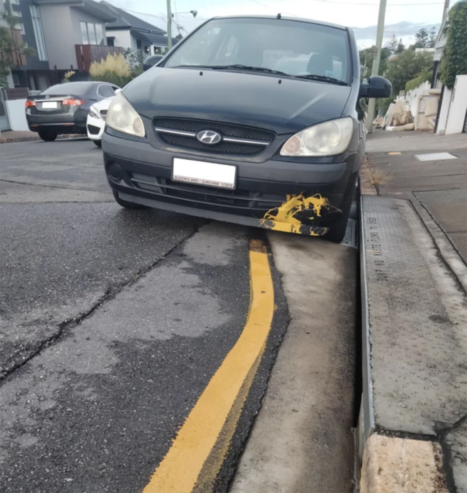 The black Hyundai with yellow paint on is bumper parked on the side of the Brisbane road. 