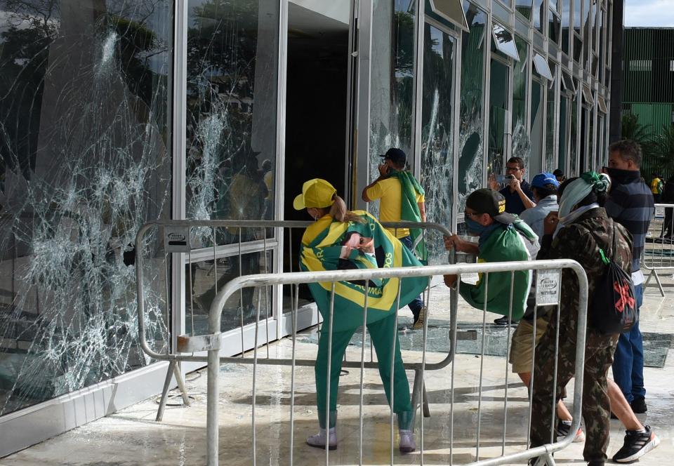 Supporters of Brazilian former President Jair Bolsonaro destroy a window from an outside deck, which has a few barricades..