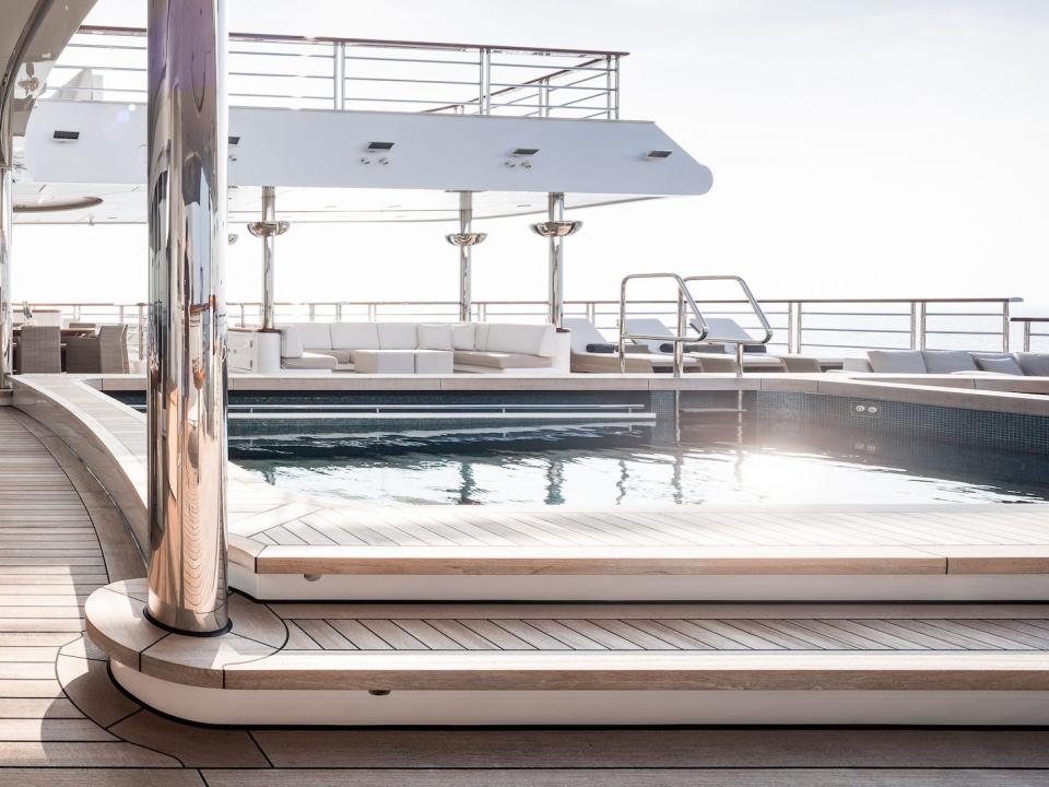 The pool on an outdoor deck next to a long dining table.