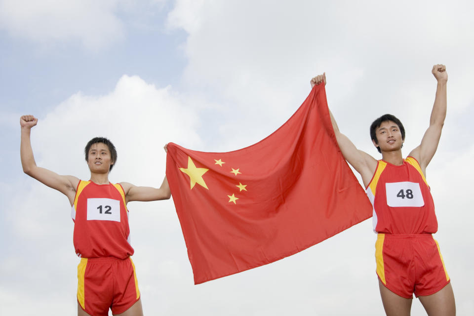 Two Chinese athletes holding a Chinese flag between them.