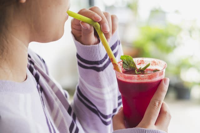 <p>Sutthiwat Srikhrueadam / Getty Images</p> An individual drinking a cup of vibrant red beet juice through a green straw.