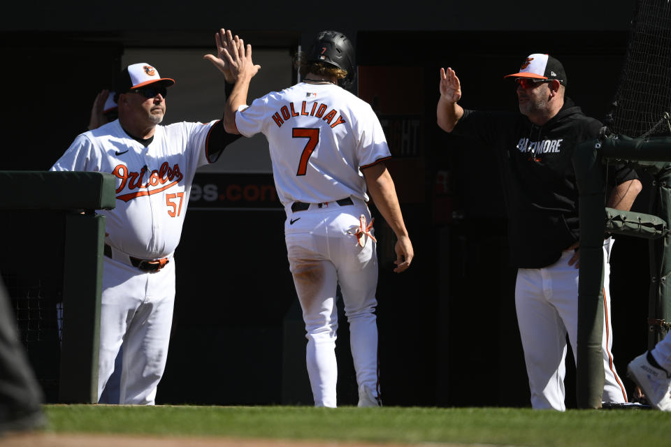 Baltimore Orioles' Jackson Holliday (7) is greeted by bench coach Fredi González (57) and manager Brandon Hyde, right, after he scored on a groundout by Adley Rutschman during the seventh inning of a baseball game against the Milwaukee Brewers, Sunday, April 14, 2024, in Baltimore. (AP Photo/Nick Wass)