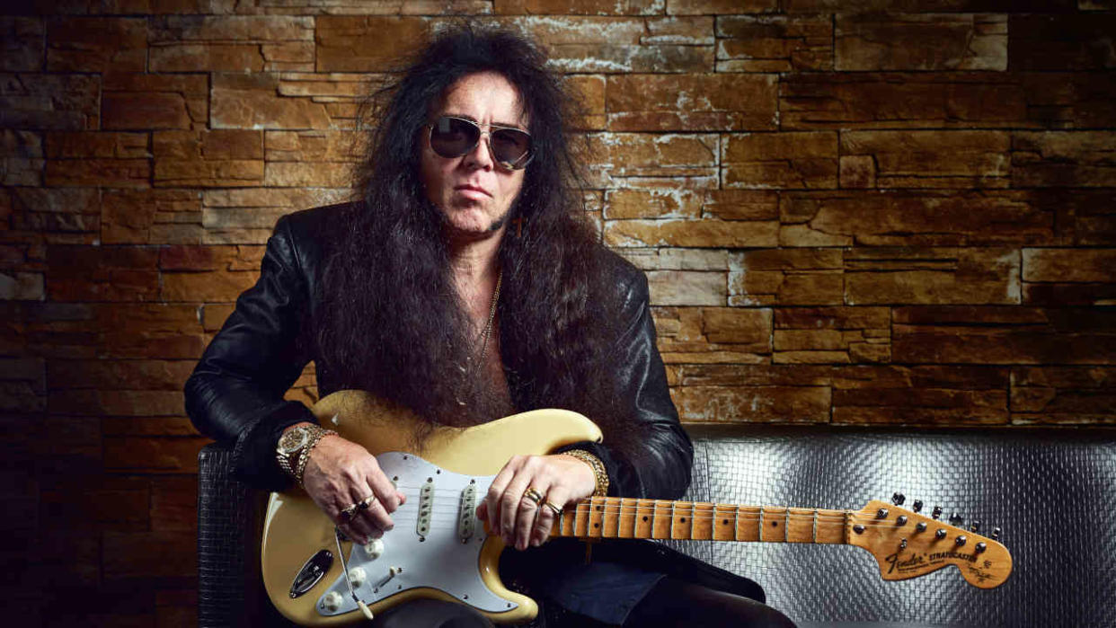  Yngwie Malmsteen holding his guitar sitting on a couch. 