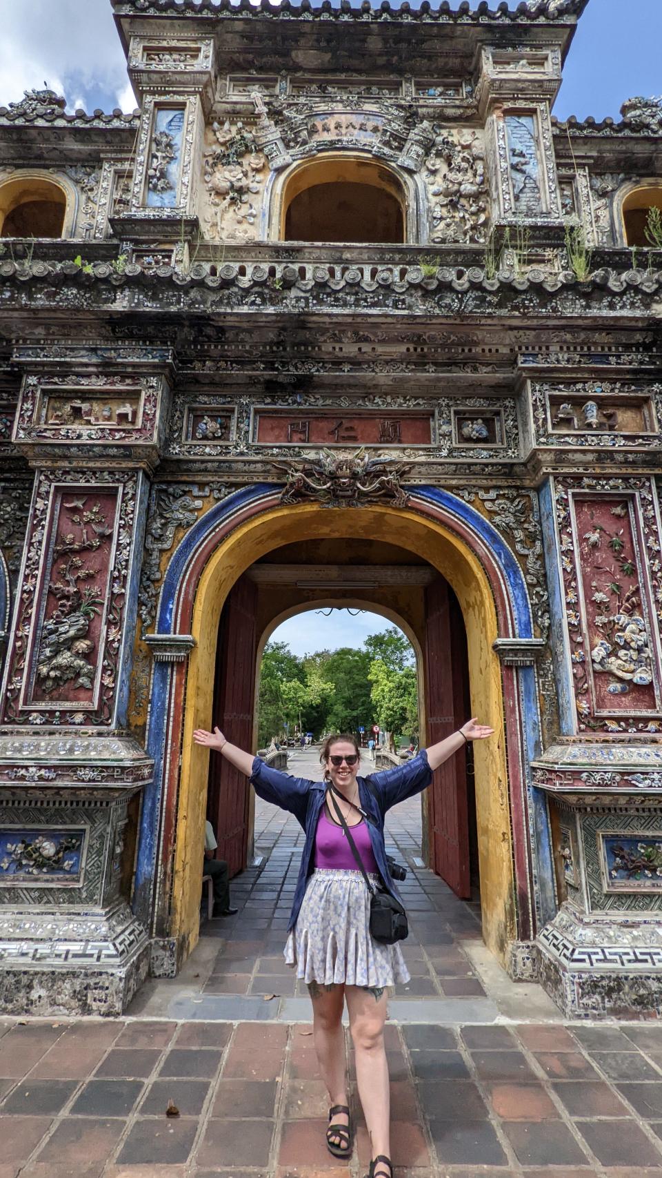 A woman poses for a picture with her arms outstretched in front of an ornate temple.