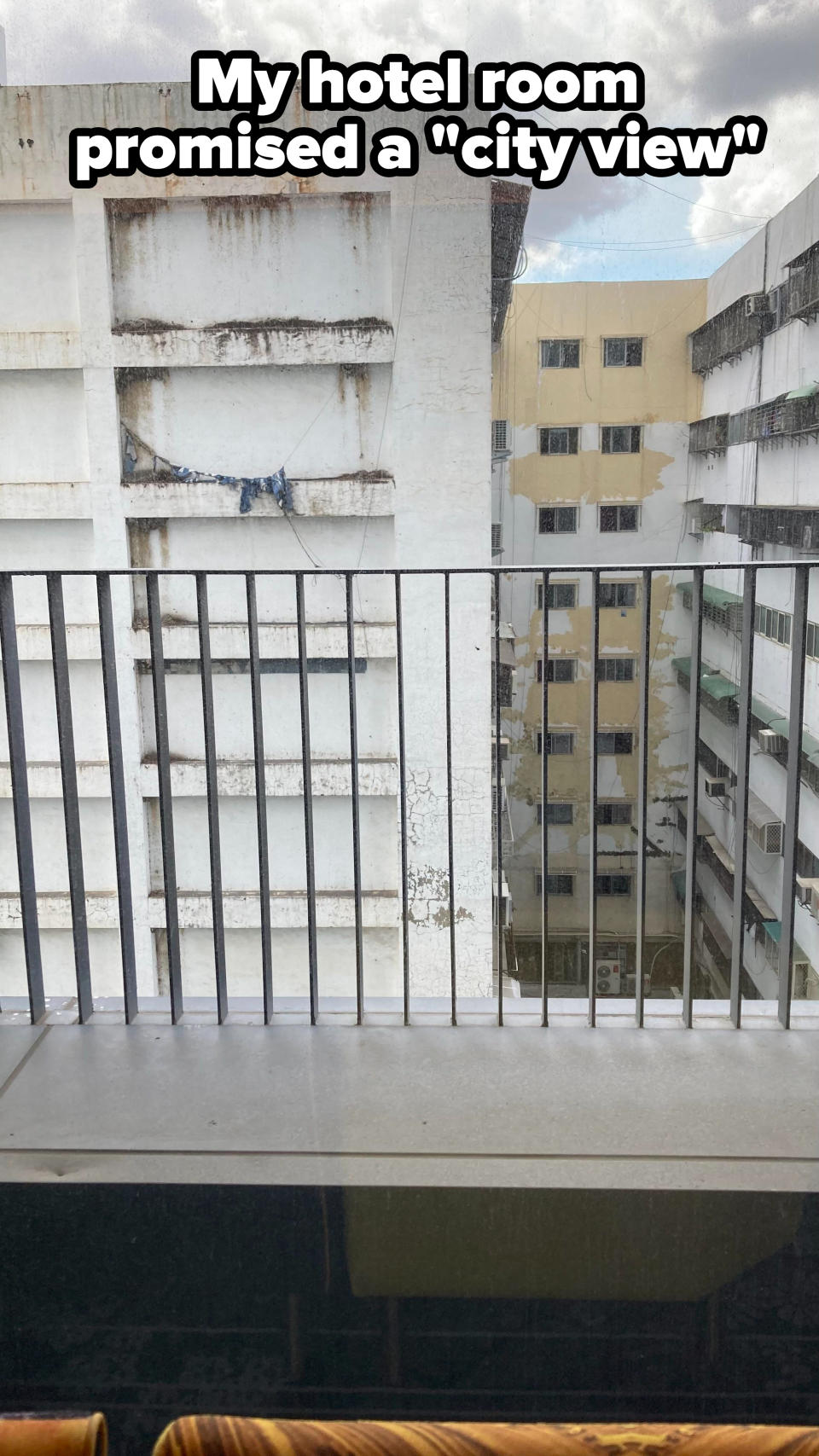 The back of a gray, nondescript, badly painted, boarded-up building seen from a balcony, with the caption "My hotel room promised a 'city view'"