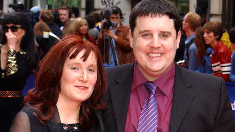 Comedian Peter Kay in a maroon shirt and suit on the red carpet with his wife Susan