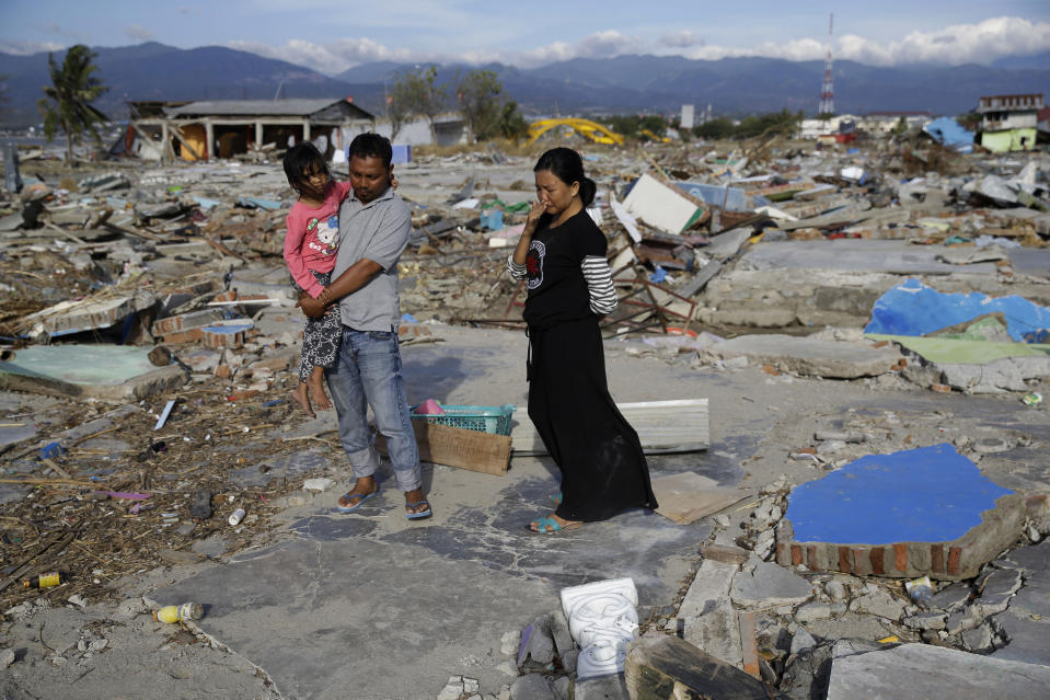 In this Oct. 5, 2018, photo, Musrifah, right, holds back tears beside her husband Hakim and daughter Syafa Ramadi as they visit where their house once stood before a massive earthquake and tsunami hit their seaside village in Palu, Central Sulawesi, Indonesia. The family lost their son. The 7.5 magnitude quake triggered not just a tsunami that leveled huge swathes of the region's coast, but a geological phenomenon known as liquefaction, making the soil move like liquid and swallowing entire neighborhoods. (AP Photo/Aaron Favila)