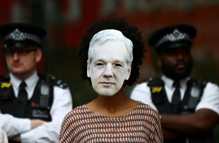 A demonstrator wearing a mask depicting Julian Assange protests as police officers stand guard outside of Westminster Magistrates Court, where a case hearing for U.S. extradition of Wikileaks founder Julian Assange is held, in London