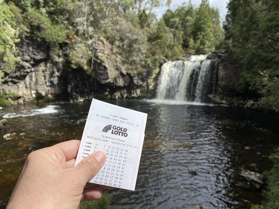 Person holding Lotto ticket in front of Australian waterfall. Source: The Lott