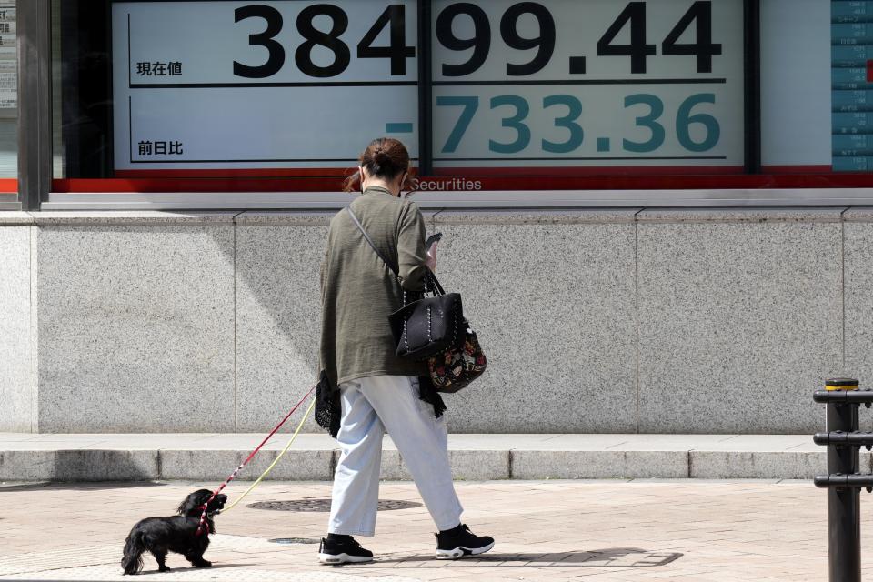 A person strolls with a dog in front of an electronic stock board showing Japan's Nikkei 225 index at a securities firm Tuesday, April 16, 2024, in Tokyo. (AP Photo/Eugene Hoshiko)