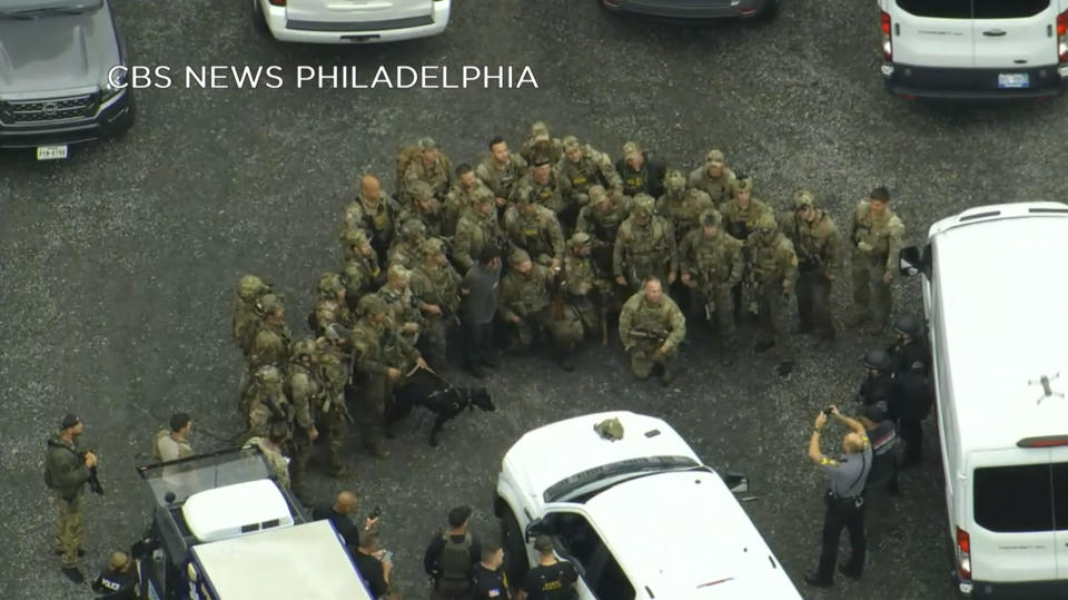 In this image from video provided by CBS NEWS Philadelphia, law enforcement officers pose for a group photo with Danelo Cavalcante after his capture in rural Pennsylvania on Wednesday, Sept. 13, 2023. The murderer who brazenly escaped from a Pennsylvania jail was captured in the woods by a team of tactical officers, bringing an end to an intensive search that terrified residents as the fugitive broke into homes for food, changed his appearance and stole a van and rifle during two weeks on the run. (CBS NEWS Philadelphia KYW-TV via AP)