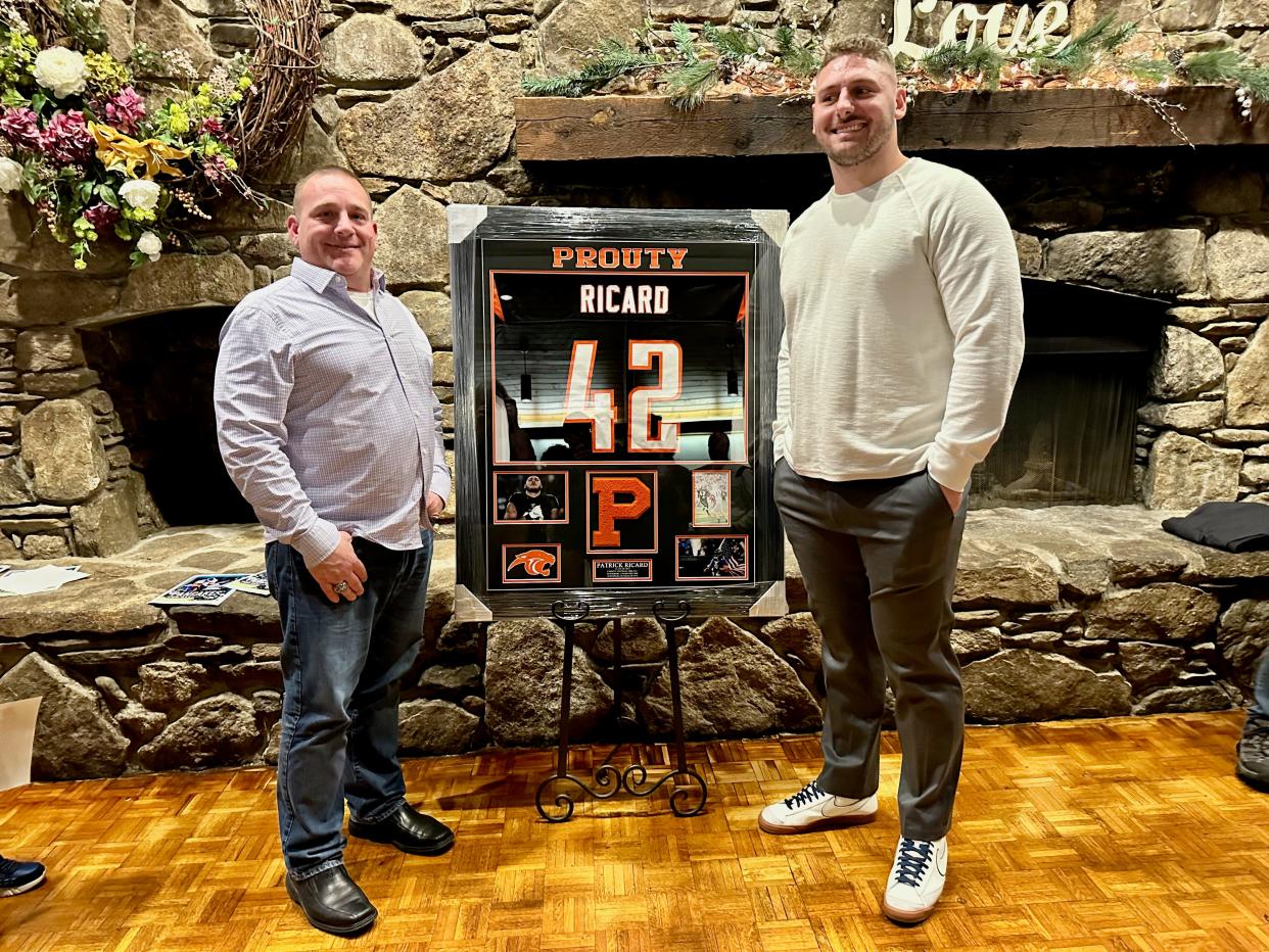 Former David Prouty football star Pat Ricard, right, now playing for the Baltimore Ravens, stands with his former coach, Andrew Tuccio, in front of Ricard's  No. 42 jersey that has been retired by the school and will hang in the new gymnasium at David Prouty.