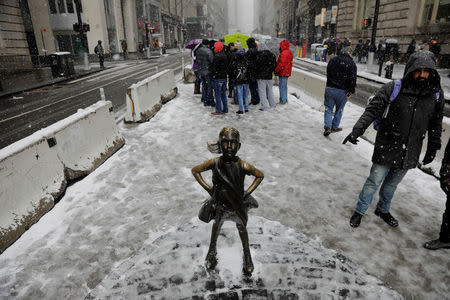 Pedestrians walk past a snow covered "Fearless Girl" sculpture during a late season nor'easter in New York, U.S., March 21, 2018. REUTERS/Lucas Jackson