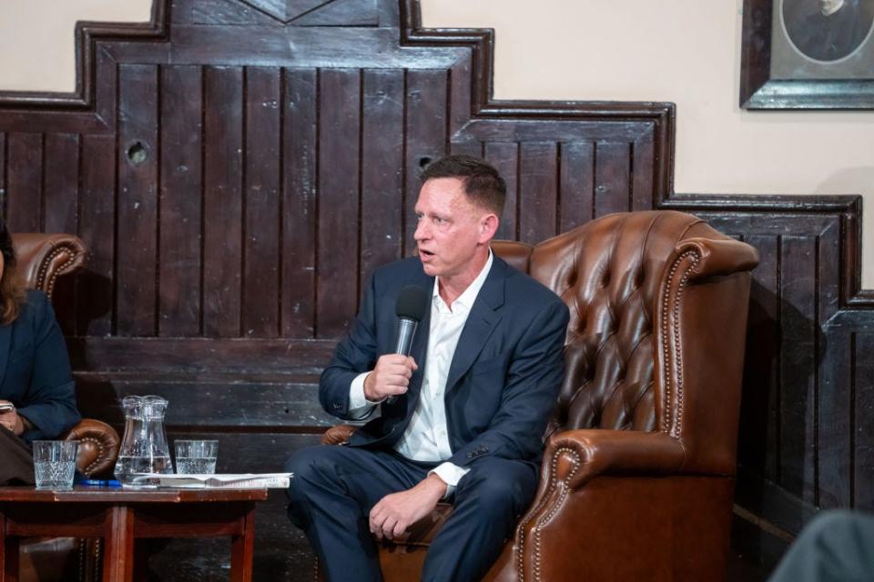 Peter Thiel holding a microphone and sitting in a chair at the Cambridge University Union