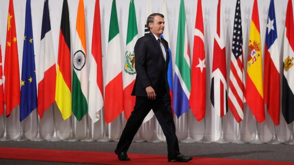 Jair Bolsonaro caminha em frente a bandeiras de países do G20 durante encontro do grupo em 2019